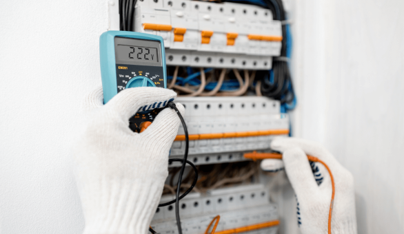 Gloved hands using a digital multimeter to test a circuit breaker panel