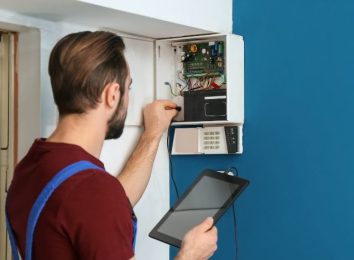 Electrician using a tablet while testing a wall-mounted control panel