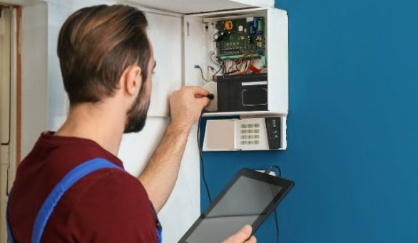 Electrician using a tablet while testing a wall-mounted control panel