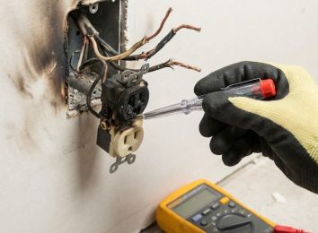 Close-up of a damaged, overheated electrical outlet being inspected with a multimeter