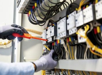 Gloved hands testing wiring inside an open breaker panel
