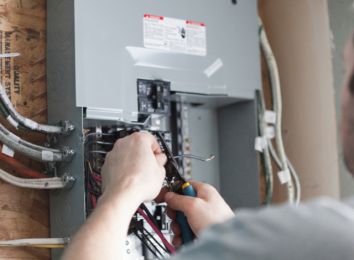 Close-up of hands wiring a gray electrical breaker panel