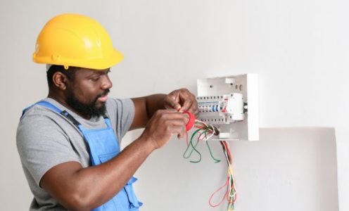 Electrician in a hard hat testing wiring on a wall panel