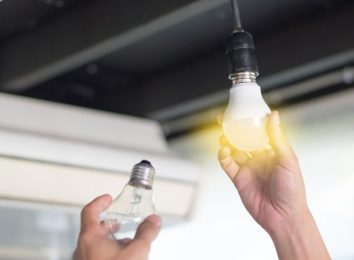 Hand holding a glowing light bulb up to a ceiling fixture