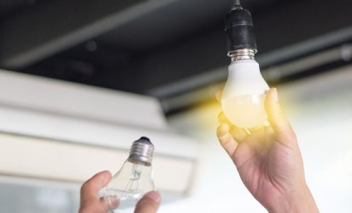 Hand holding a glowing light bulb up to a ceiling fixture