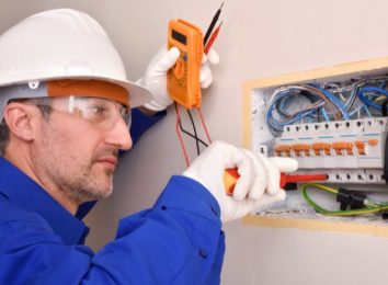 Electrician in safety glasses testing an open electrical panel