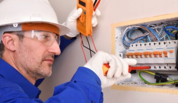 Electrician in safety glasses testing an open electrical panel