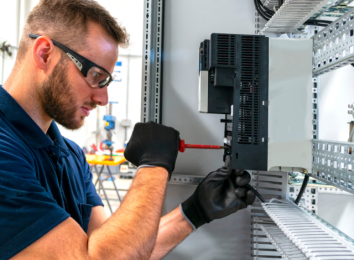 Electrician working on a wiring rack wearing safety glasses and gloves