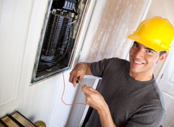 Smiling electrician in a hard hat working on an open electrical panel
