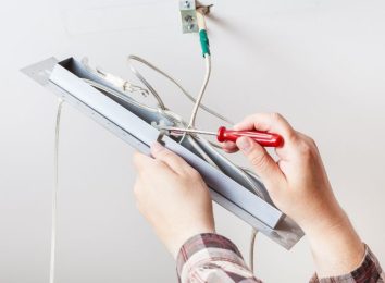 Electrician repairing a fluorescent light fixture with a screwdriver