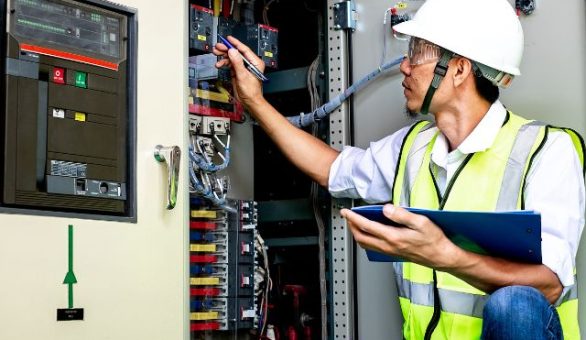 Electrician in a safety vest inspecting a commercial electrical panel with a clipboard