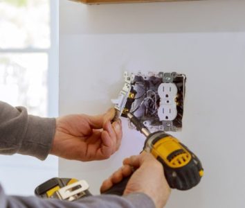 Electrician's hands installing a wall outlet with a screwdriver